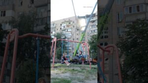 Children swing on a playground beside a building struck by a Russian attack in Kyiv on July 6